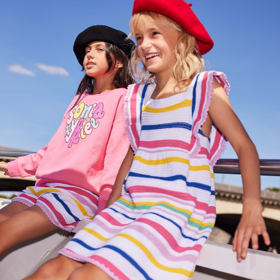 Girls wearing a multicolored striped dress and a pink sweatshirt