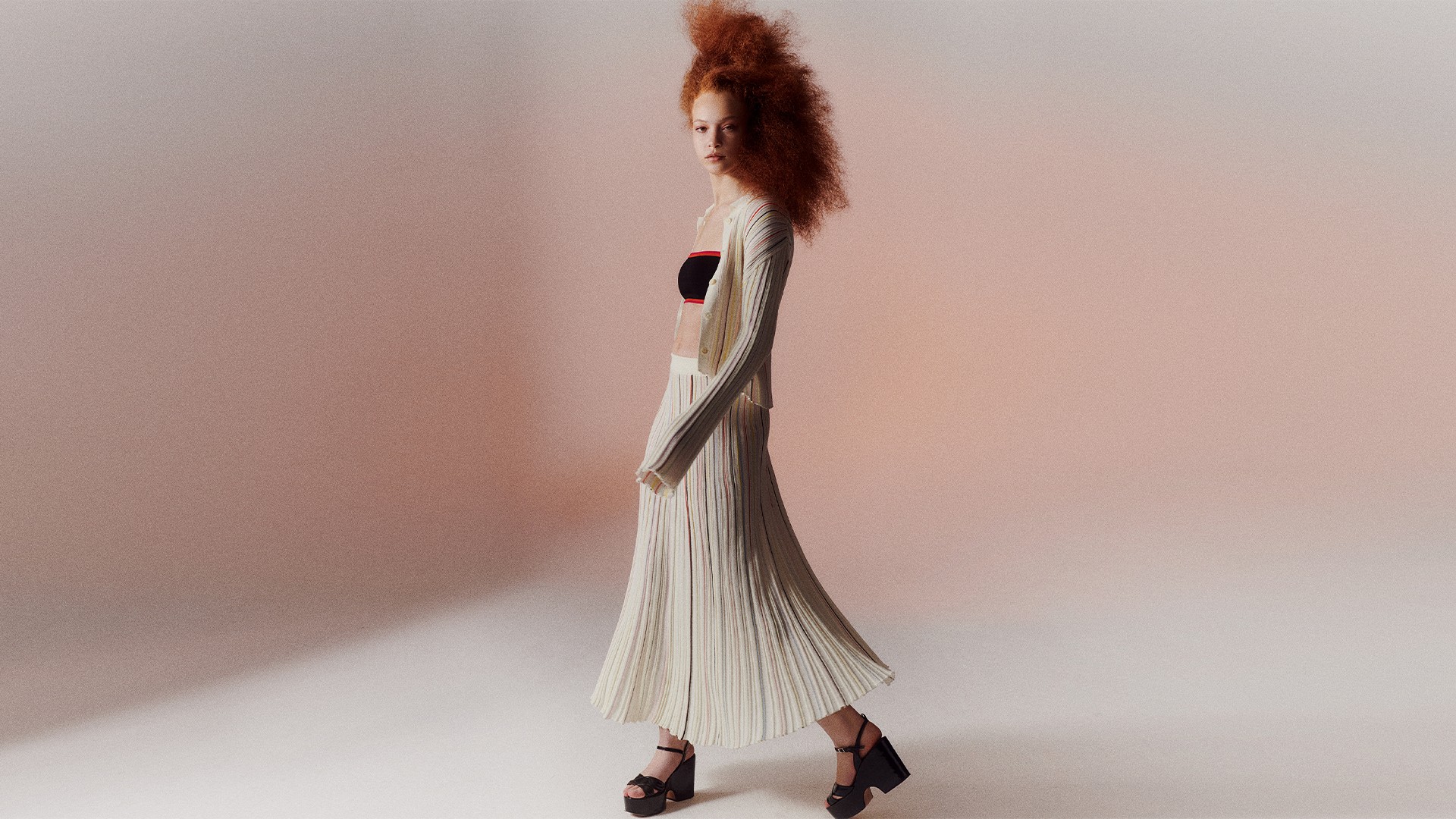 A woman wearing the multicolor striped long pleated skirt with the multicolor striped pleated shirt