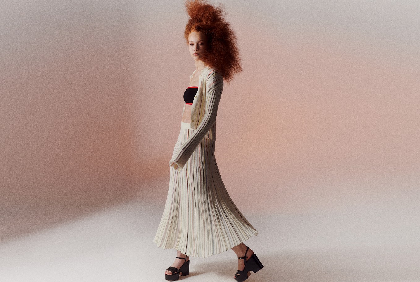 A woman wearing the multicolor striped long pleated skirt with the multicolor striped pleated shirt