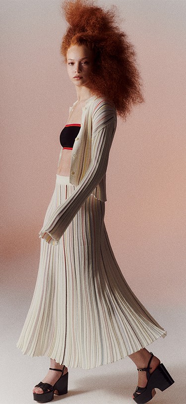 A woman wearing the multicolor striped long pleated skirt with the multicolor striped pleated shirt