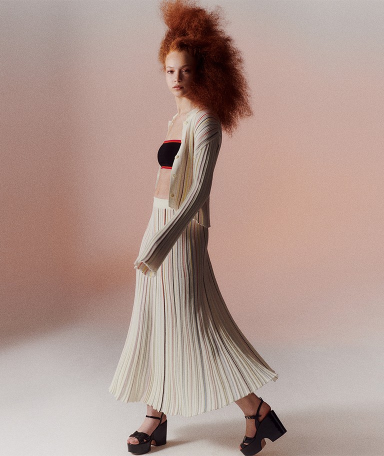 A woman wearing the multicolor striped long pleated skirt with the multicolor striped pleated shirt